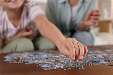 Photo of Mother and her daughter solving puzzle together at wooden table indoors, closeup