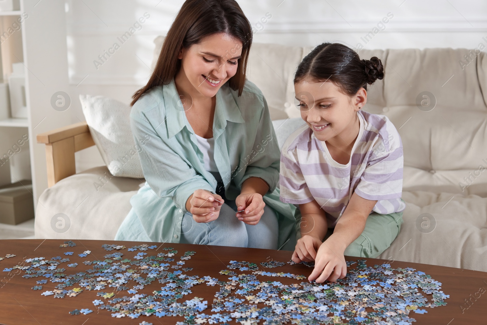 Photo of Happy mother and her daughter solving puzzle together at wooden table indoors