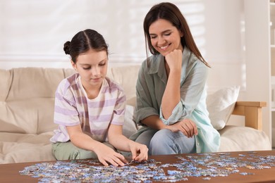 Photo of Happy mother and her daughter solving puzzle together at wooden table indoors