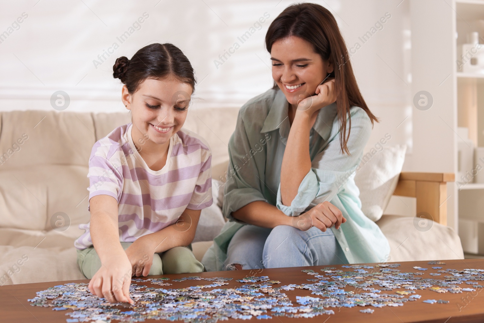 Photo of Happy mother and her daughter solving puzzle together at wooden table indoors