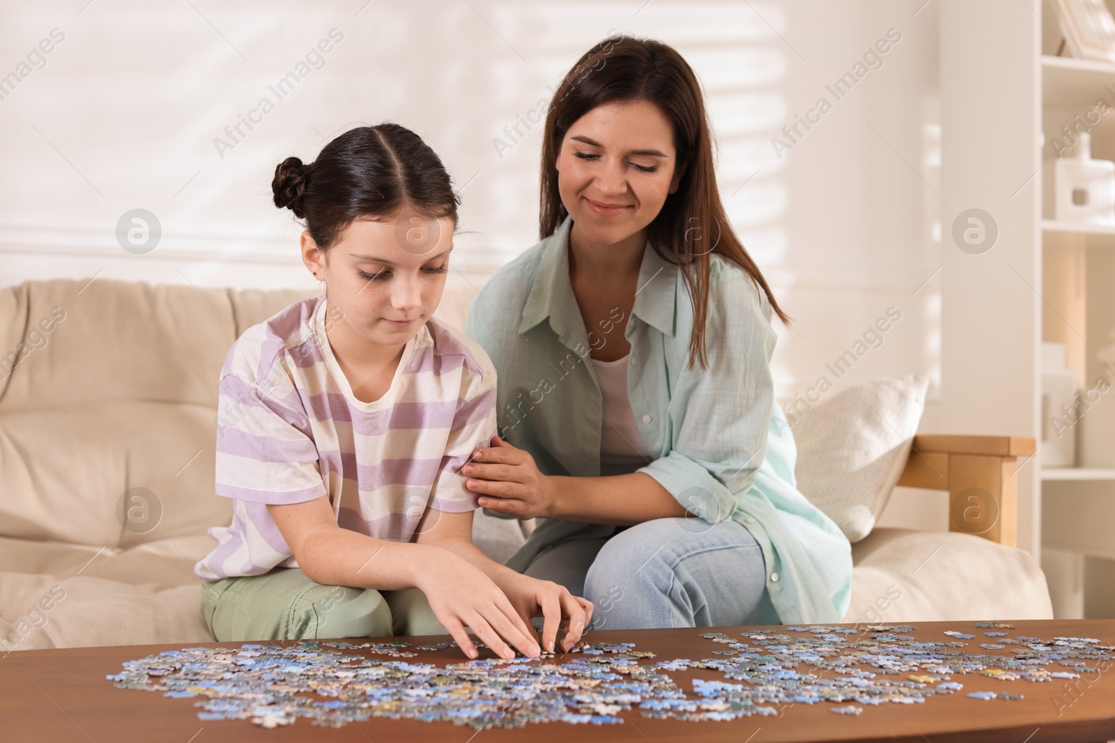 Photo of Happy mother and her daughter solving puzzle together at wooden table indoors