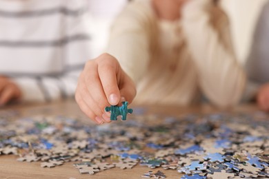 Photo of Parents and their daughter solving puzzle together at wooden table indoors, closeup