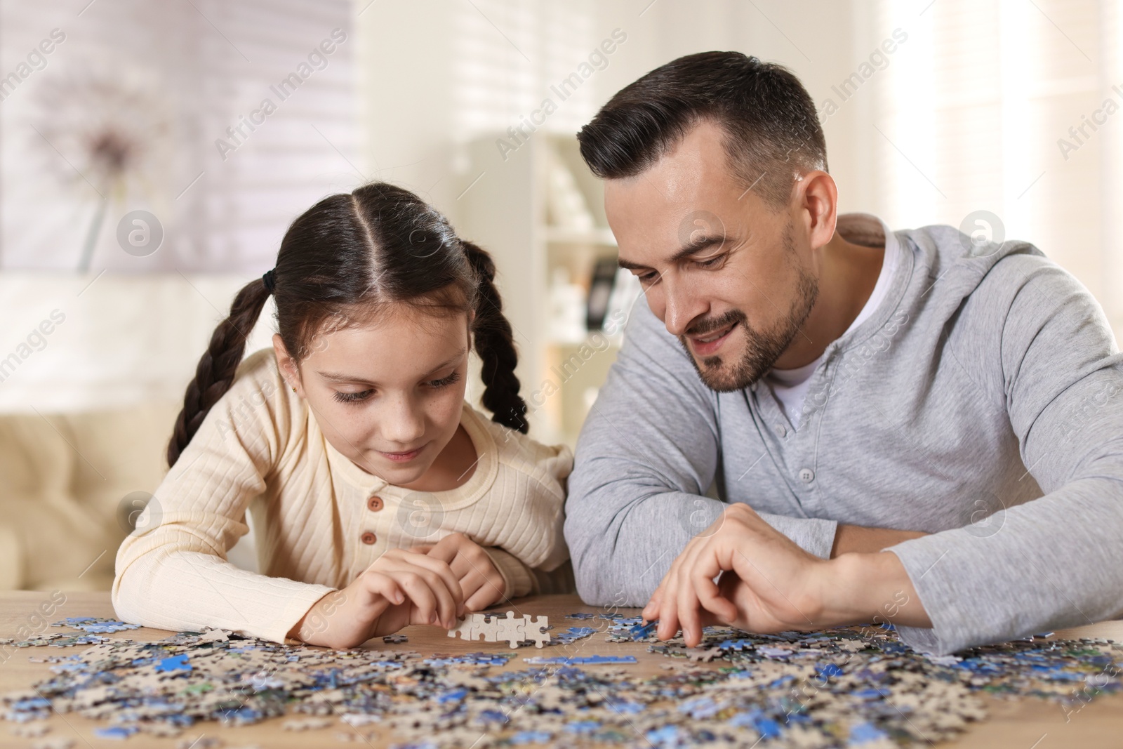 Photo of Happy father and his daughter solving puzzle together at wooden table indoors