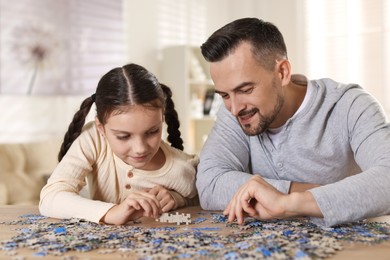 Photo of Happy father and his daughter solving puzzle together at wooden table indoors