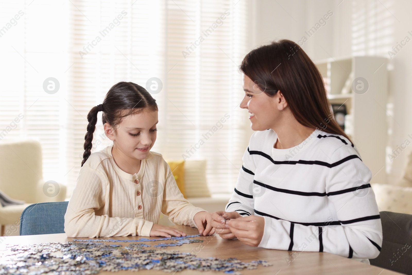 Photo of Happy mother and her daughter solving puzzle together at wooden table indoors