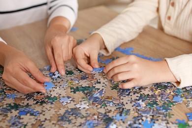 Photo of Mother and her daughter solving puzzle together at wooden table indoors, closeup