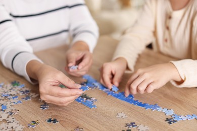 Photo of Mother and her daughter solving puzzle together at wooden table indoors, closeup