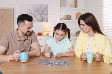 Photo of Happy parents and their daughter solving puzzle together at wooden table indoors