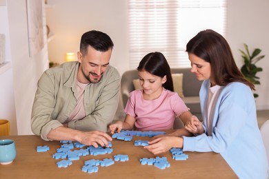 Photo of Happy parents and their daughter solving puzzle together at wooden table indoors