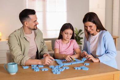 Happy parents and their daughter solving puzzle together at wooden table indoors