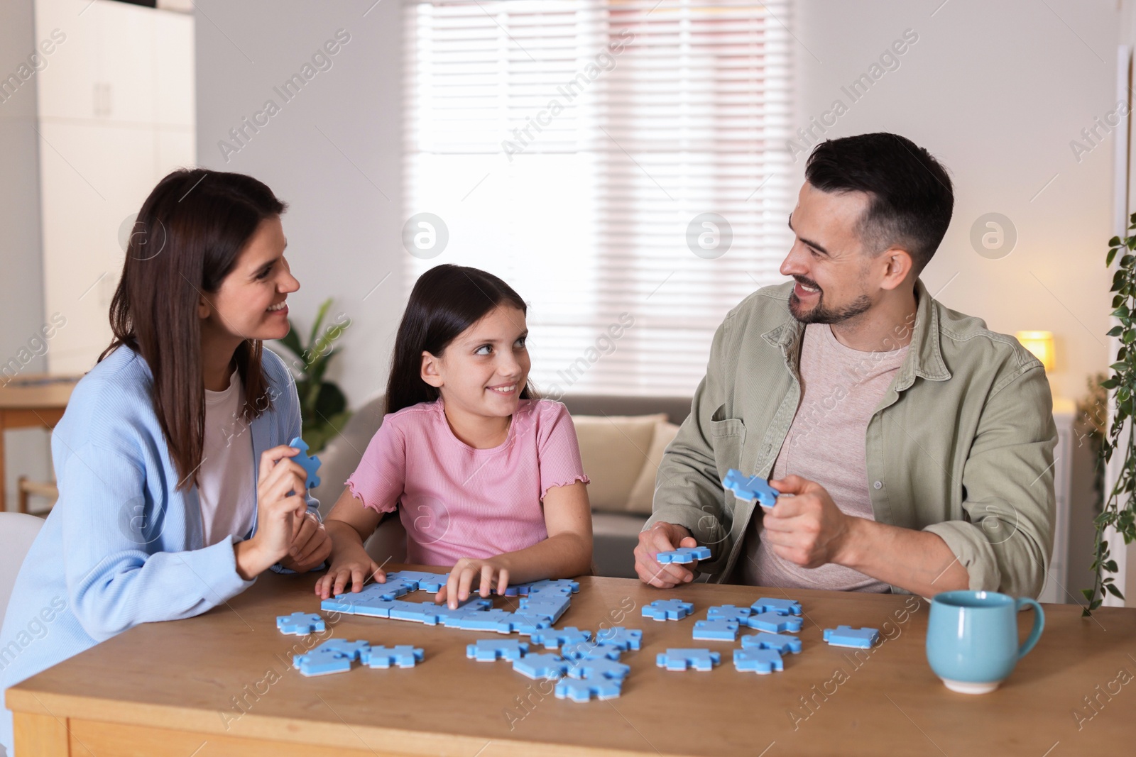 Photo of Happy parents and their daughter solving puzzle together at wooden table indoors