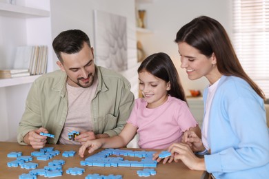 Photo of Happy parents and their daughter solving puzzle together at wooden table indoors