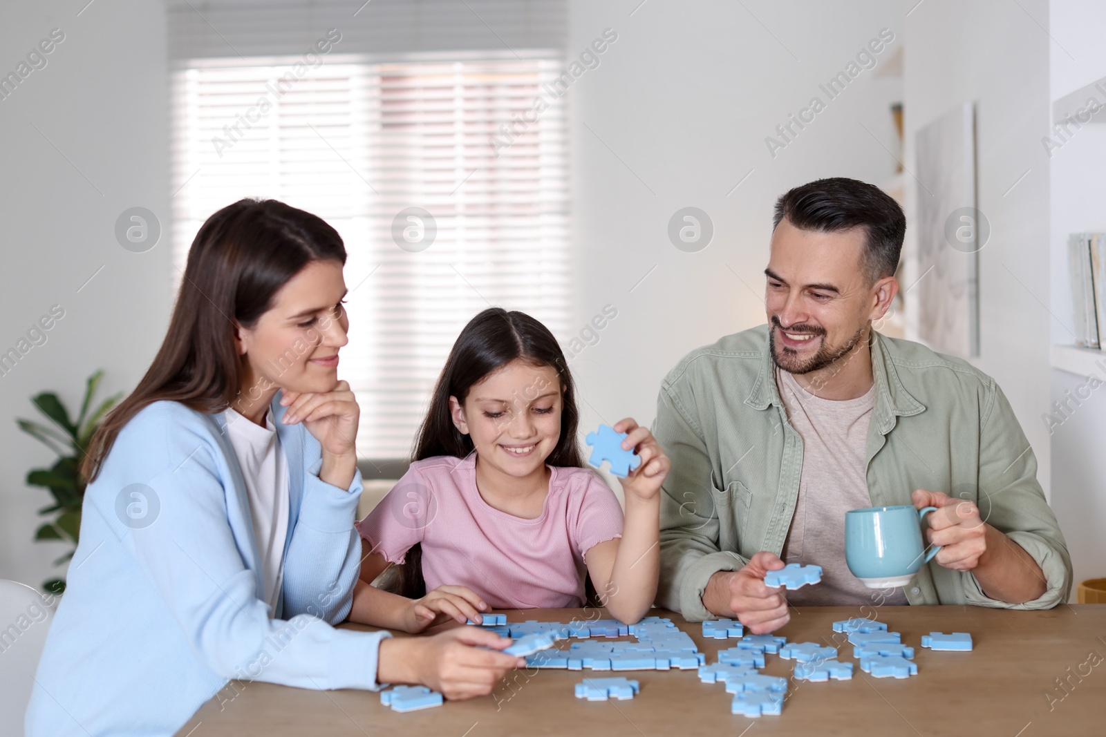 Photo of Happy parents and their daughter solving puzzle together at wooden table indoors