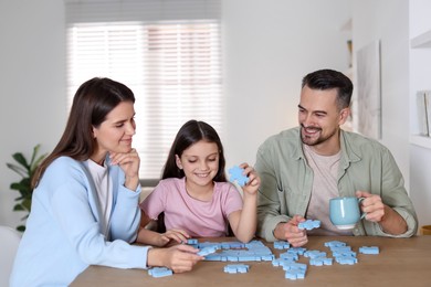 Happy parents and their daughter solving puzzle together at wooden table indoors