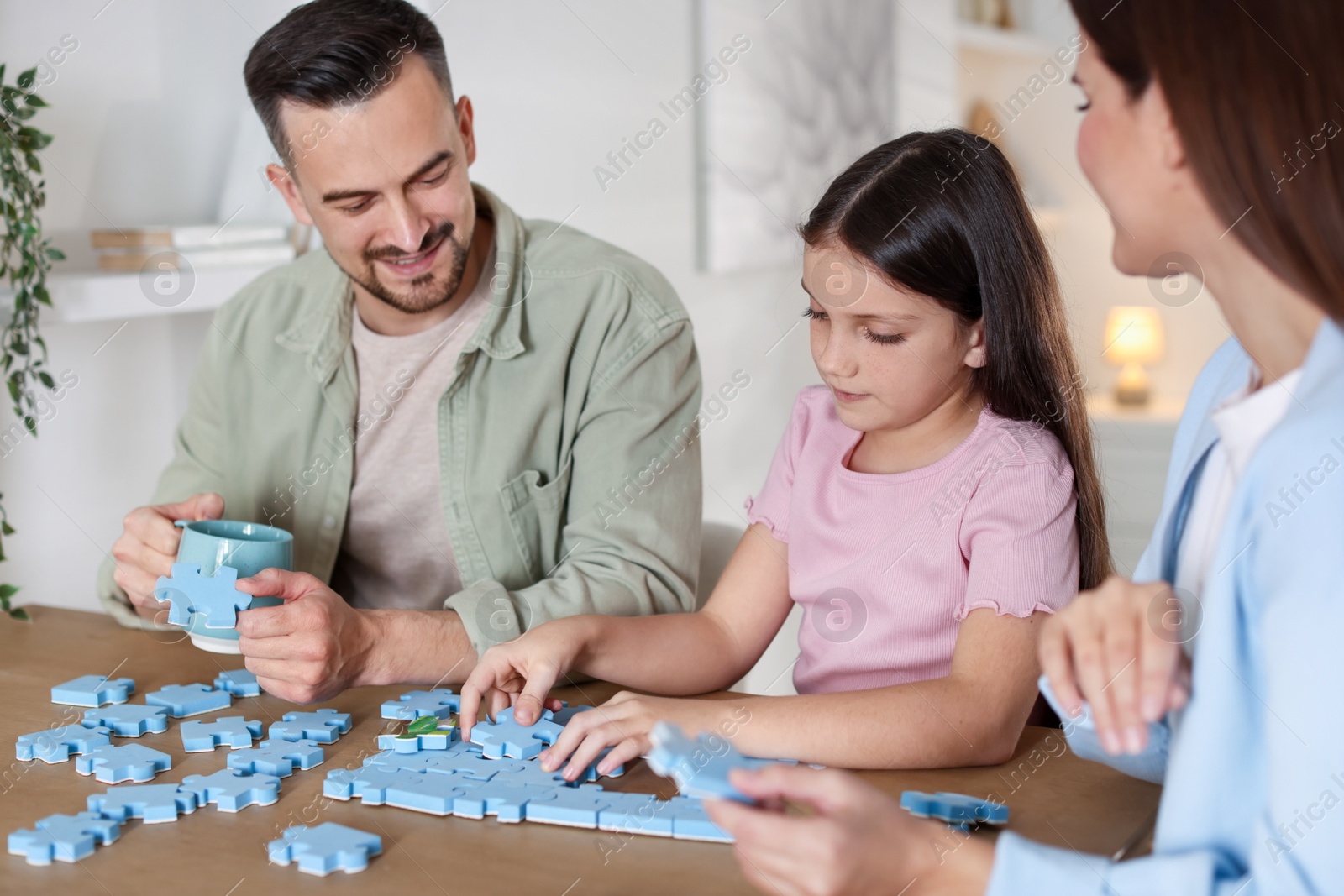 Photo of Happy parents and their daughter solving puzzle together at wooden table indoors