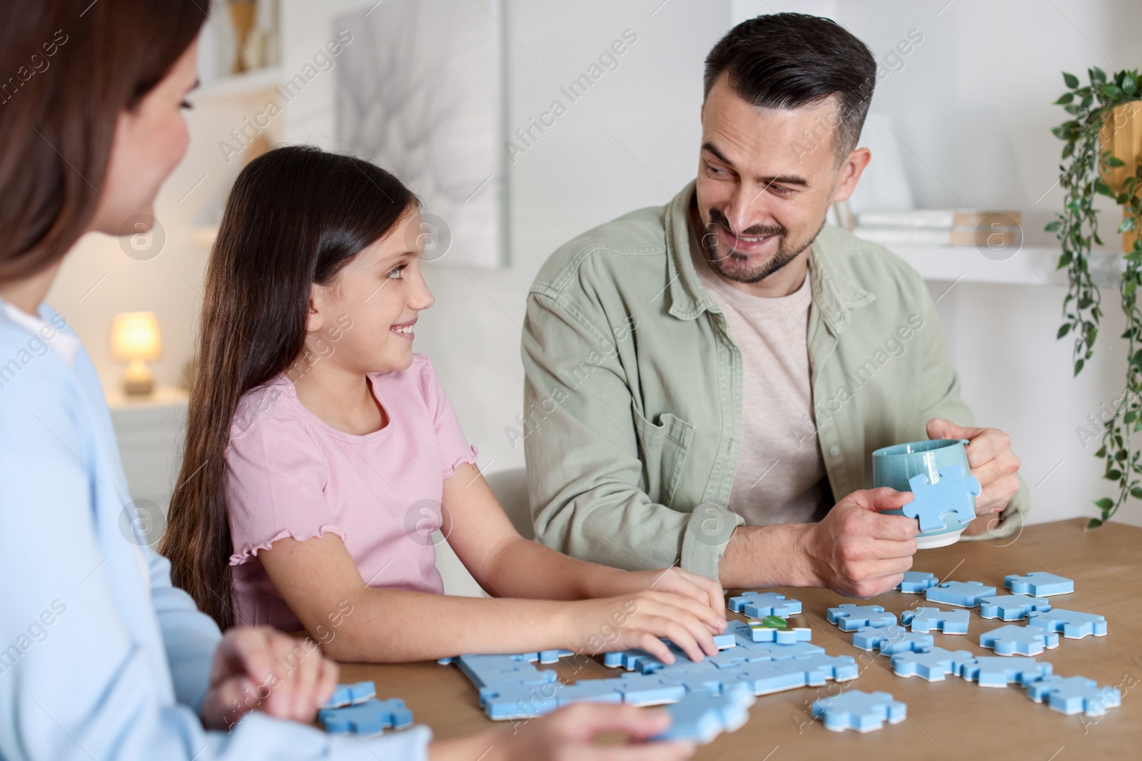 Photo of Happy parents and their daughter solving puzzle together at wooden table indoors