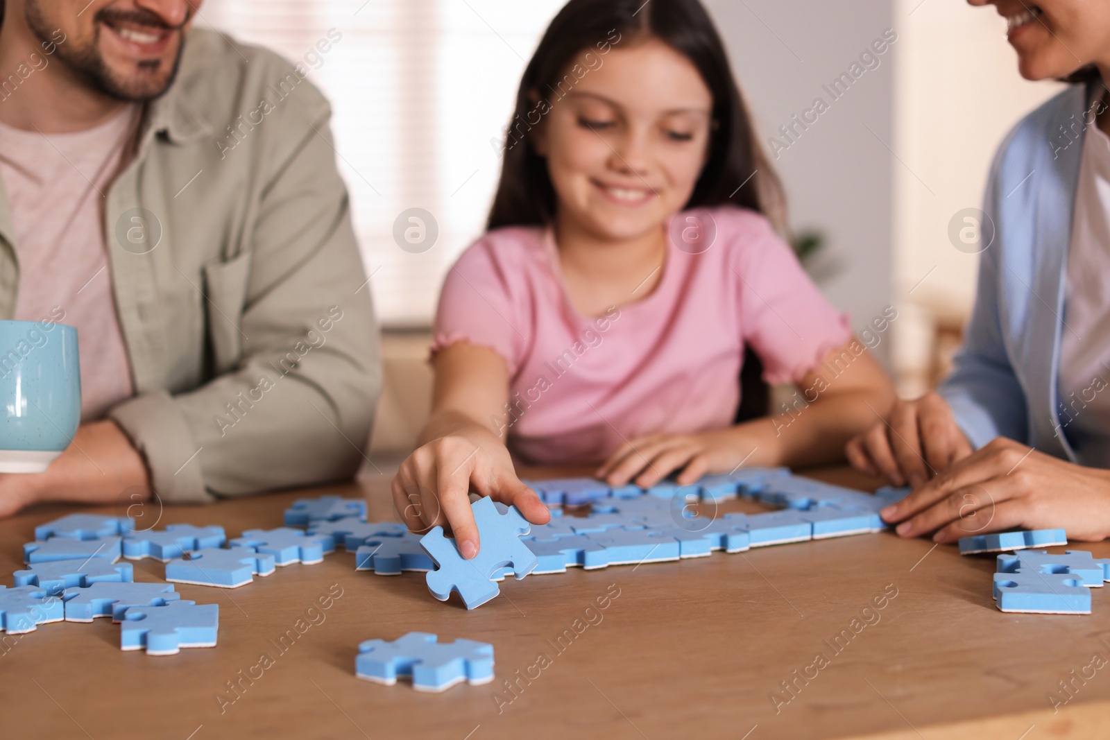 Photo of Happy parents and their daughter solving puzzle together at wooden table indoors