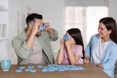 Happy parents with their daughter having fun and solving puzzle together at wooden table indoors