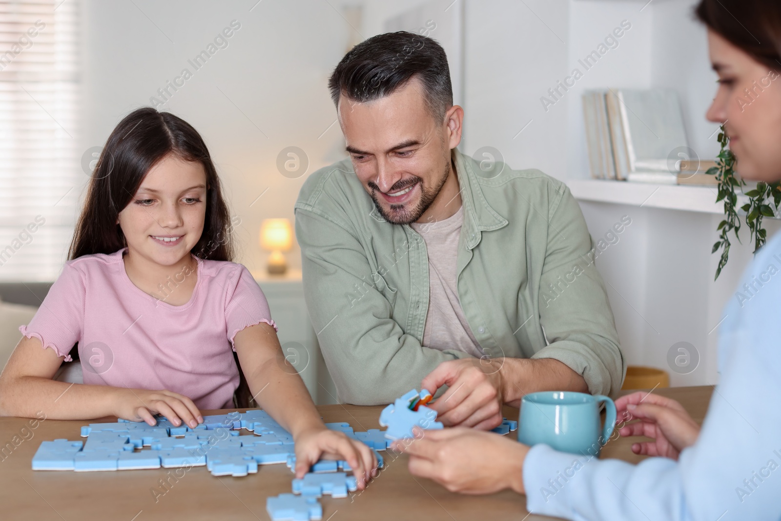 Photo of Happy parents and their daughter solving puzzle together at wooden table indoors