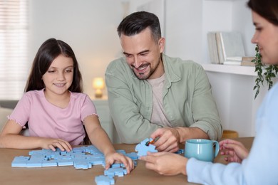 Happy parents and their daughter solving puzzle together at wooden table indoors