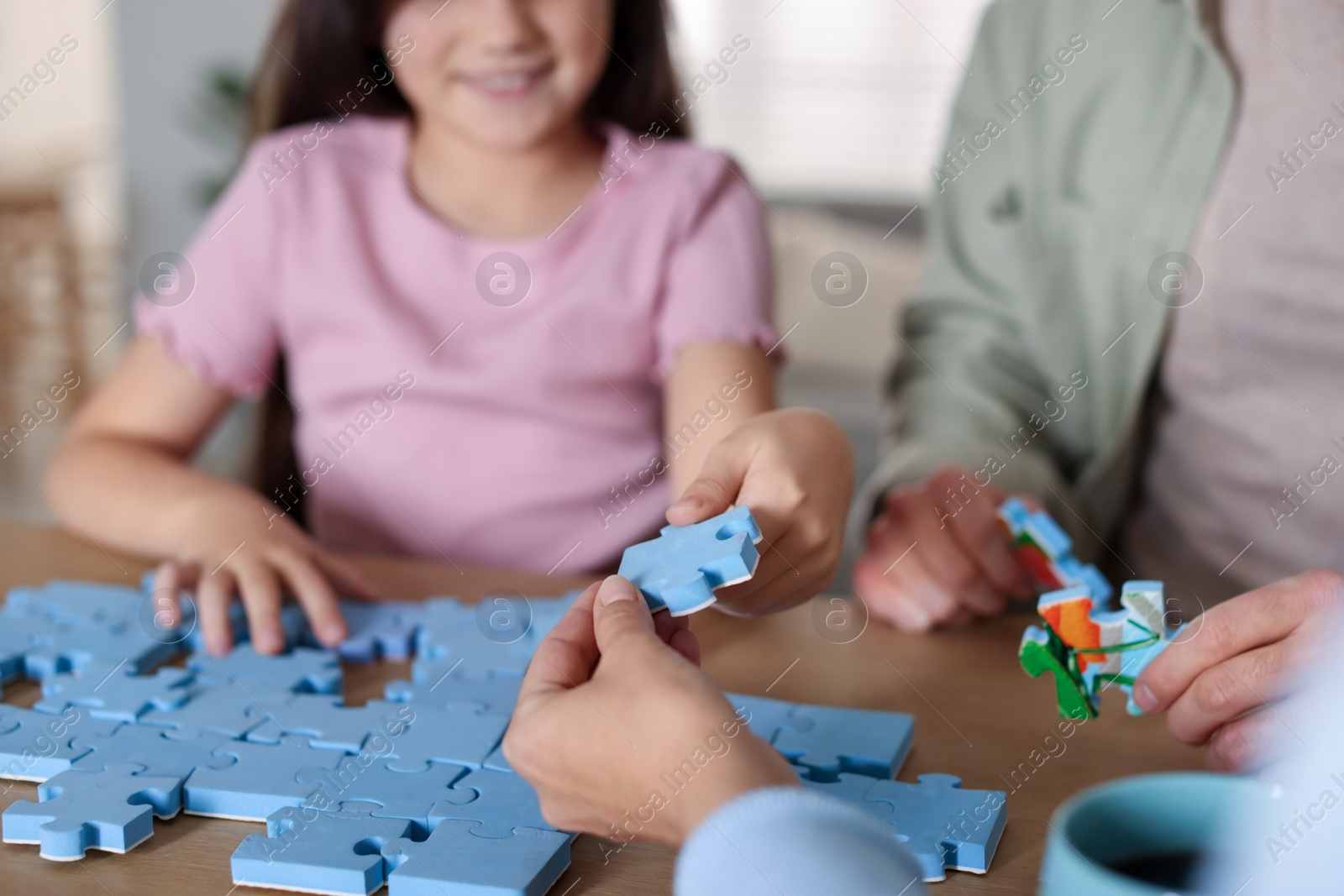 Photo of Parents and their daughter solving puzzle together at wooden table indoors, closeup