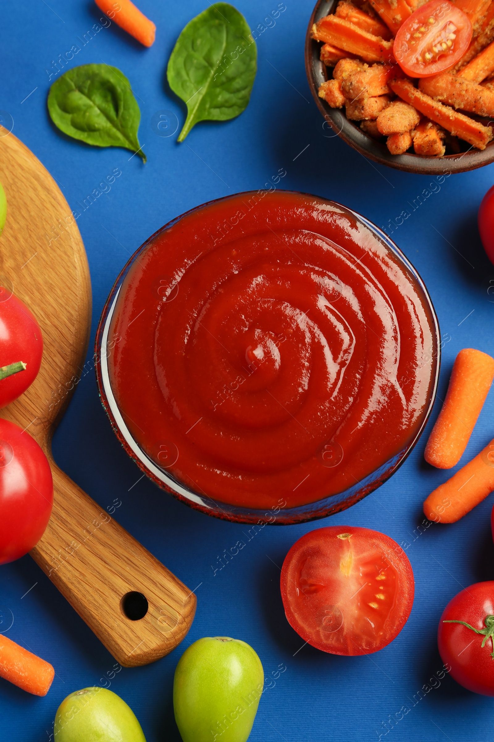 Photo of Tasty ketchup and vegetables on blue background, flat lay