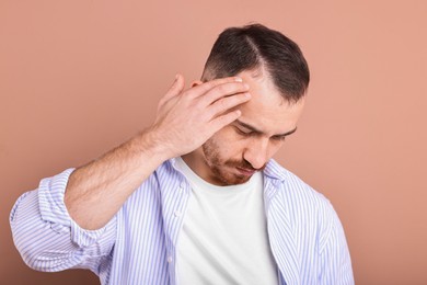 Baldness problem. Man with receding hairline on dark beige background