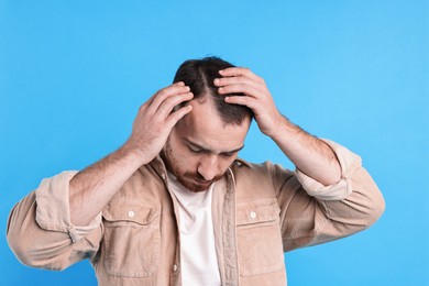 Baldness problem. Man with receding hairline on light blue background