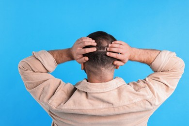 Baldness problem. Man with bald spot on light blue background, back view