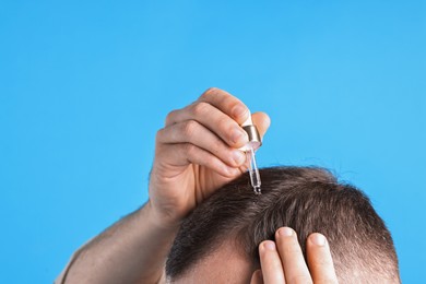 Photo of Baldness problem. Man applying serum onto hairline on light blue background, closeup