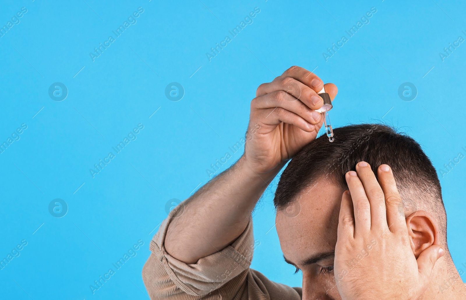 Photo of Baldness problem. Man applying serum onto hairline on light blue background, closeup. Space for text