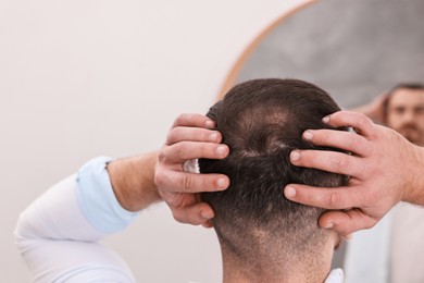 Photo of Baldness problem. Man with receding hairline near mirror in bathroom, back view