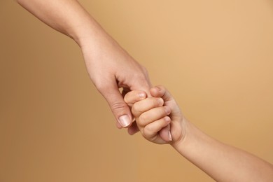 Photo of Mother and child holding hands on beige background, closeup