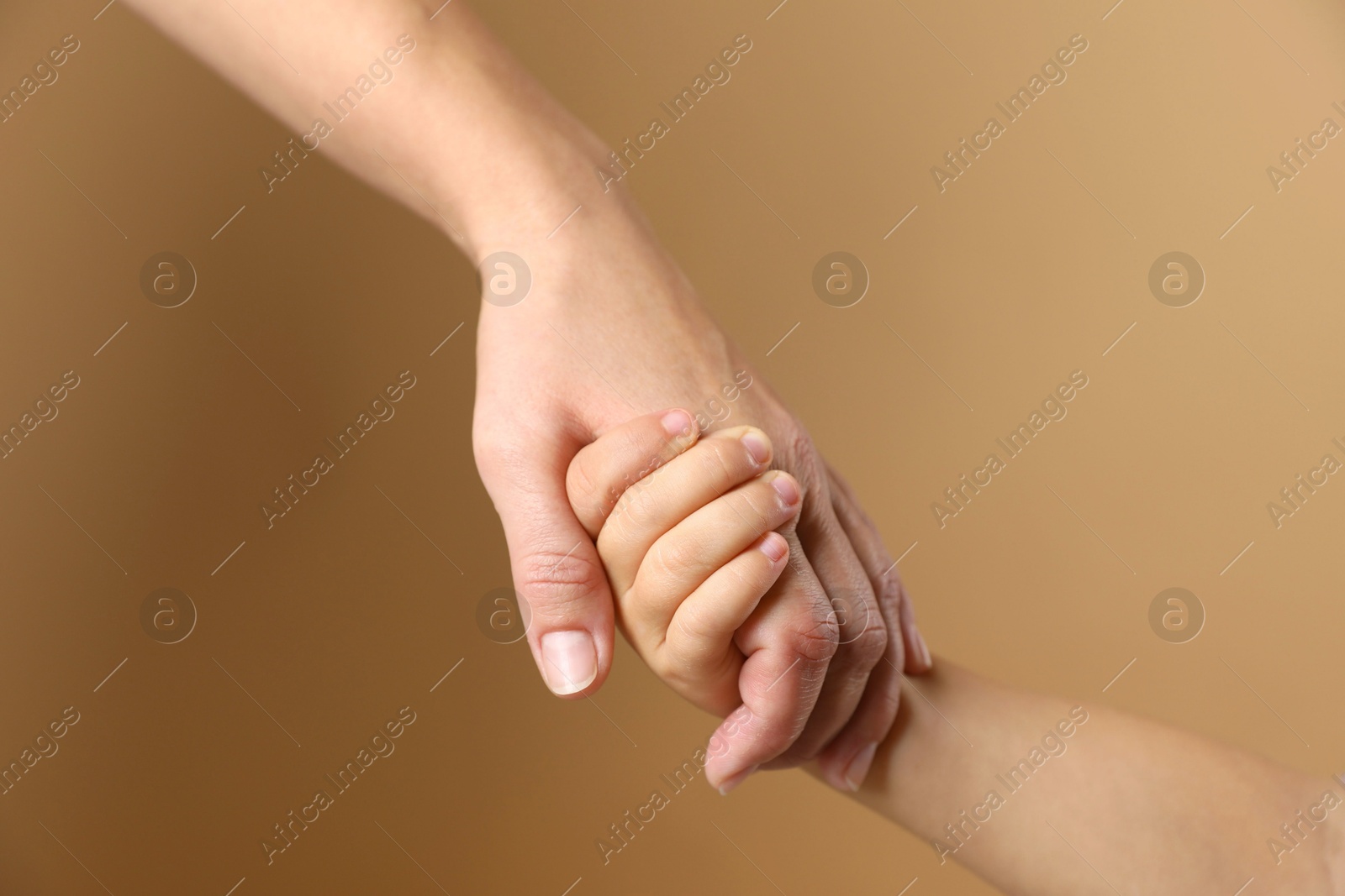 Photo of Mother and child holding hands on beige background, closeup