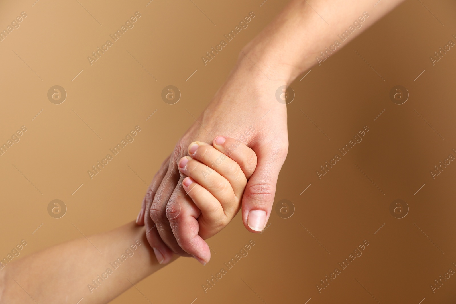 Photo of Mother and child holding hands on beige background, closeup