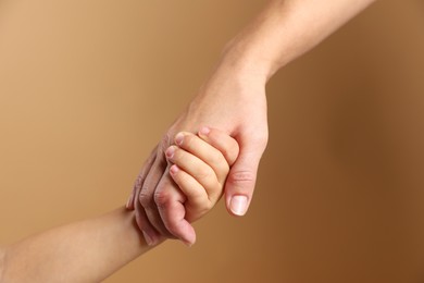 Photo of Mother and child holding hands on beige background, closeup