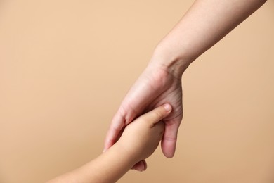 Photo of Mother and child holding hands on beige background, closeup