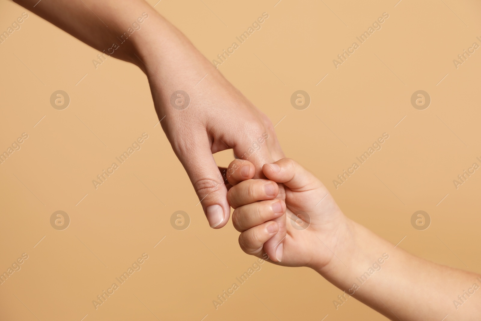 Photo of Mother and child holding hands on beige background, closeup