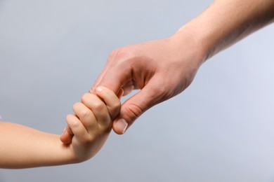 Photo of Father and child holding hands on grey background, closeup