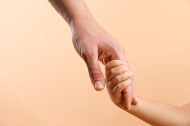 Photo of Father and child holding hands on beige background, closeup