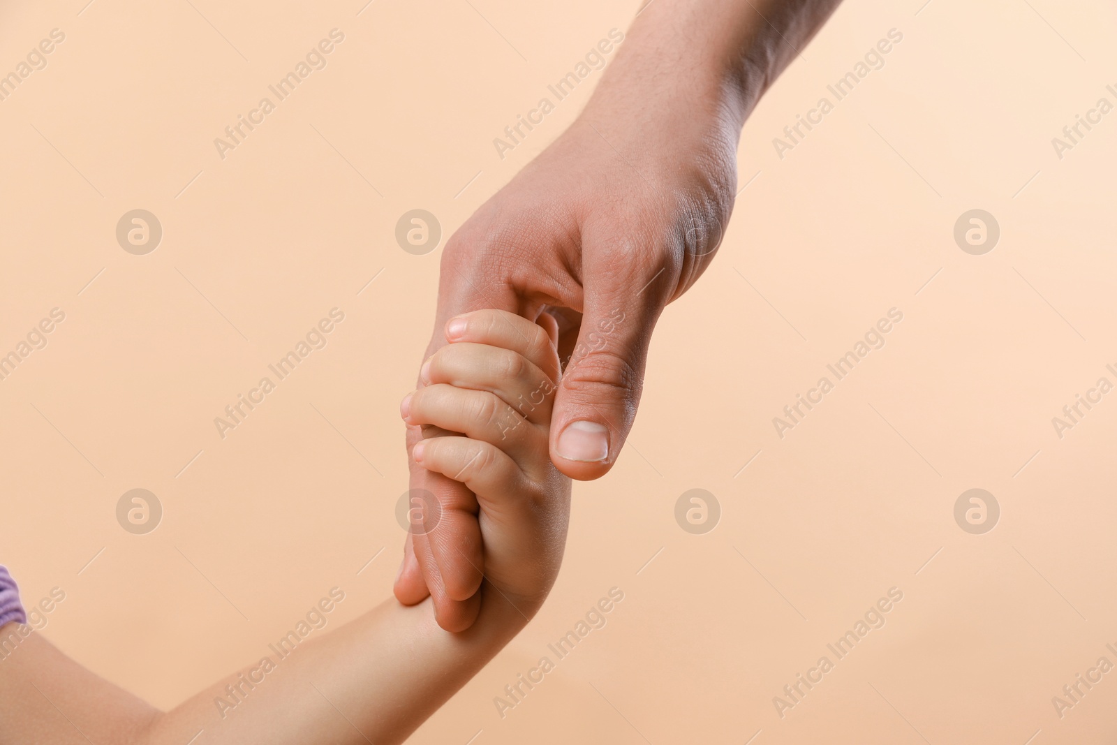 Photo of Father and child holding hands on beige background, closeup