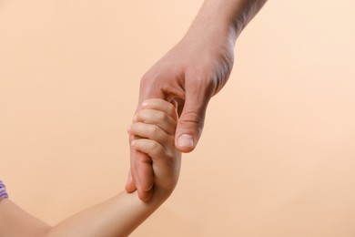 Photo of Father and child holding hands on beige background, closeup