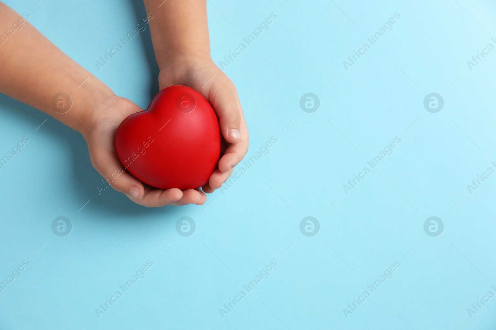 Photo of Child holding decorative red heart on light blue background, top view. Space for text