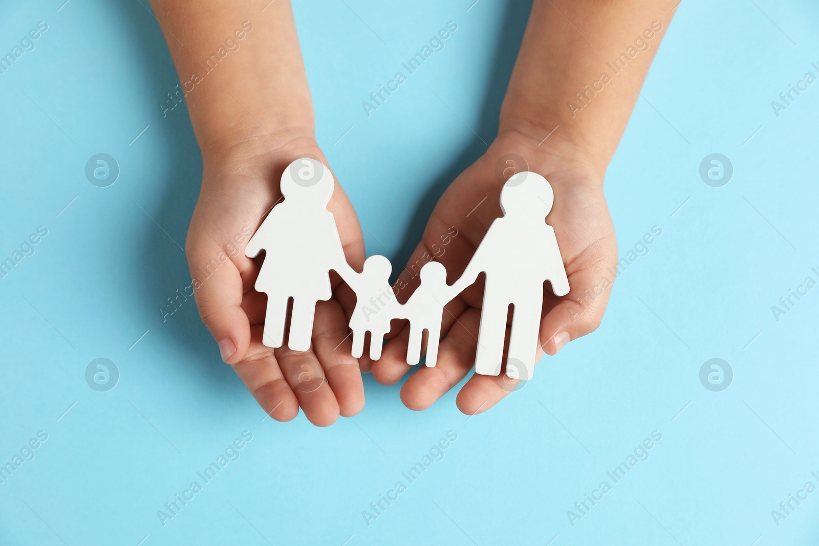 Photo of Child holding figure of family on light blue background, top view