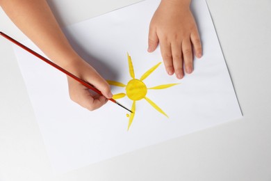 Photo of Little child drawing sun with paint at light table, top view