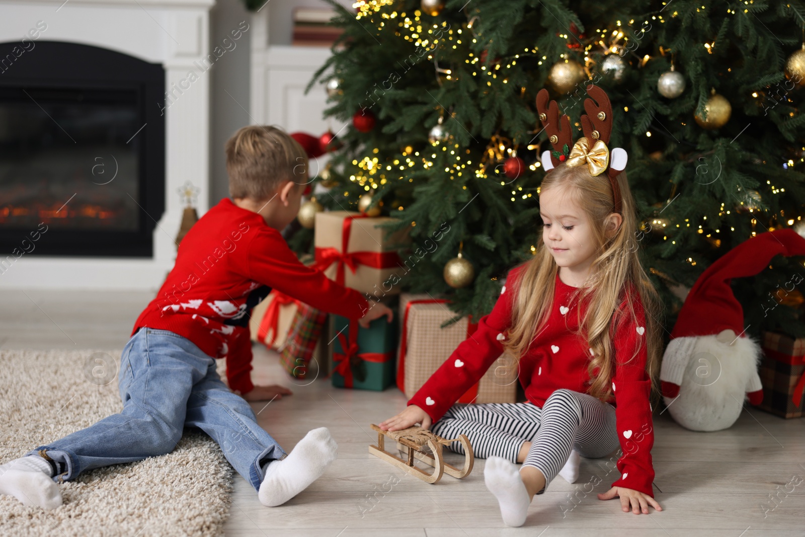 Photo of Little children with gifts near Christmas tree at home