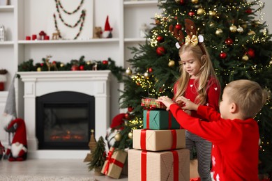 Little children with gifts near Christmas tree at home. Space for text