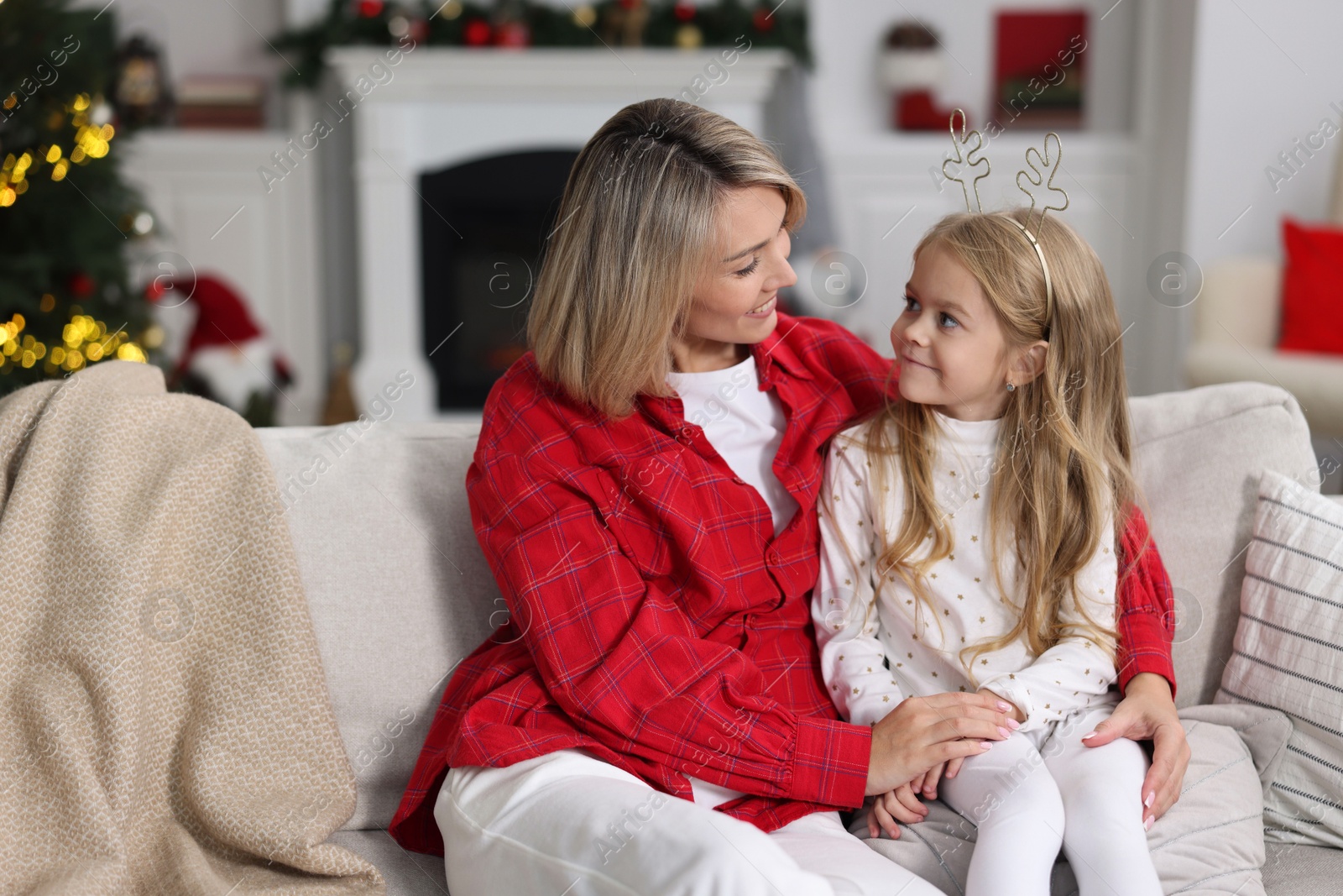 Photo of Cute little girl with her mom on sofa against Christmas lights