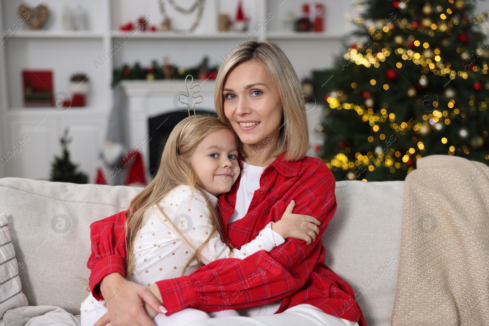 Photo of Cute little girl with her mom on sofa against Christmas lights