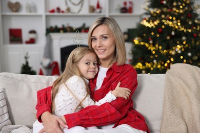 Photo of Cute little girl with her mom on sofa against Christmas lights